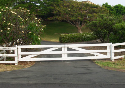 A white three rail double gate and fence surrounded by trees.